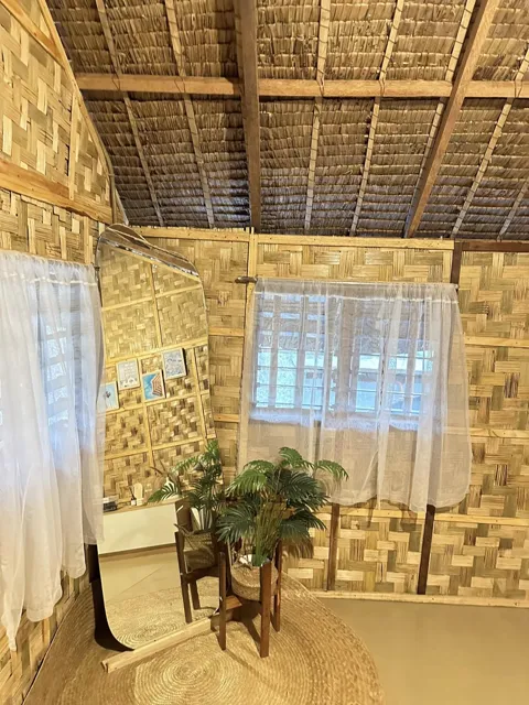 Woven bamboo walls, a curtained window, and a potted plant.